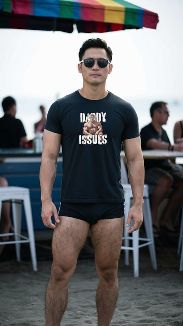 Man in black t-shirt with text 'Daddy Issues' at beach bar, wearing sunglasses.