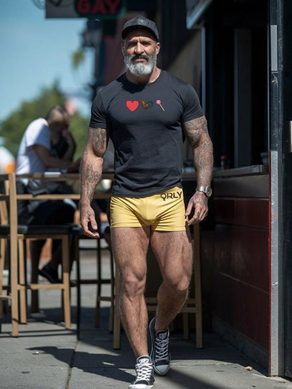 Muscular man in gay pride apparel, black funny gay t-shirt, yellow shorts, walking outdoors.