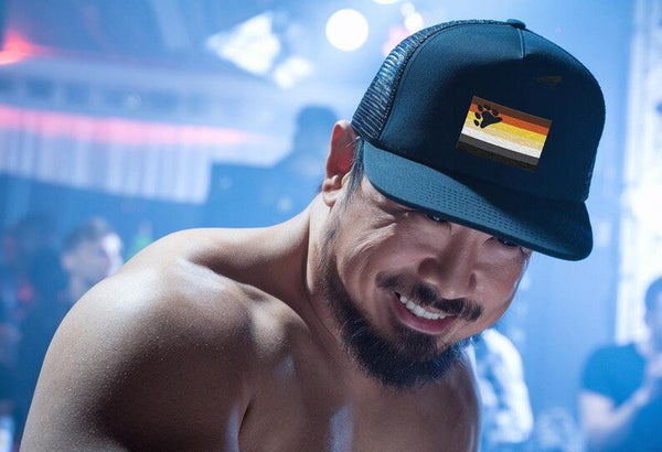 Model wearing a black Gay Bear Trucker Hat with bear graphic, showcasing gay pride apparel.