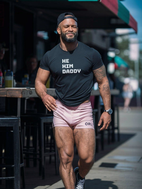 He/Him Daddy Shirt Gay Bear Pride T-Shirt for Men LGBTQ+ Queer Apparel, muscular man wearing black tee and pink shorts.