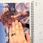 hand holding a raunchy gay beefcake calendar featuring a muscular nude man in a snowy mountain scene