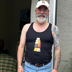 gay bear man wearing a black tank top with a cute bear pride graphic standing indoors