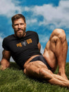 Model wearing a black Proud Gay Bear - Gay Pride Shirt outdoors on grassy field.