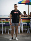 Model wearing Proud Pig Shirt – Gay Bear Shirt, with beach and rainbow bar backdrop.
