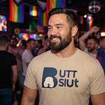 bearded gay man wearing a beige butt slut shirt in a crowded queer nightclub with pride flags in the background, fun raunchy lgbt vibe