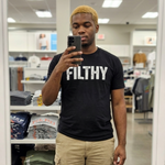 man taking a mirror selfie wearing a black ‘Filthy’ QRLY Merch t-shirt in a clothing store