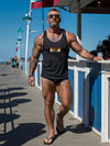 Muscular man wearing black tank top with bear pride flag design by beach.