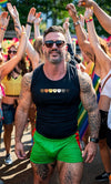 Muscular man in gay bear tanktop at pride event, surrounded by colorful celebration.