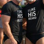 “gay couple wearing matching humorous shirts at an outdoor pride beach event, one reading ‘I like his butt’ and the other ‘I like his beard’.
