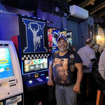 man wearing a abstract gay art t-shirt standing in a leather bar arcade area with neon lights
