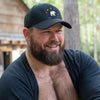 Man smiling in black Gay Pride Bear Bear Paw Hat outdoors, showcasing LGBTQ bear pride theme.
