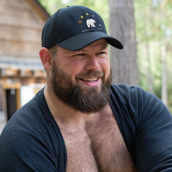 Man smiling in black Gay Pride Bear Bear Paw Hat outdoors, showcasing LGBTQ bear pride theme.